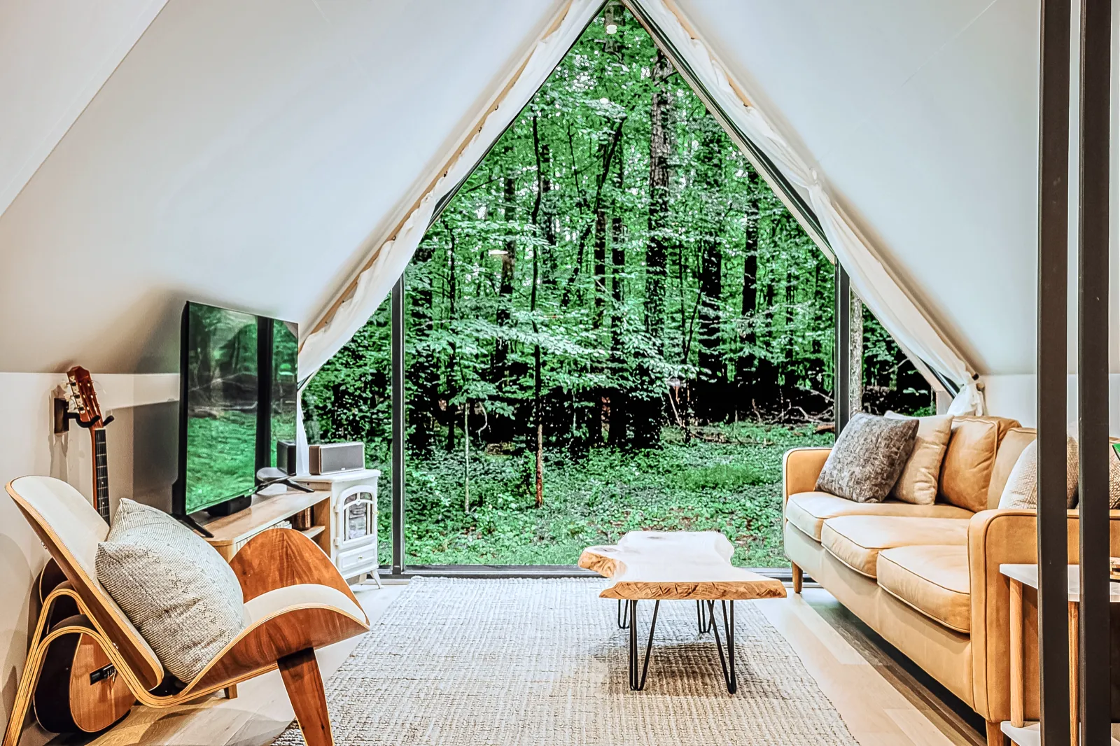 A-frame living room with leather sofa and a full triangular glass wall framing the forest