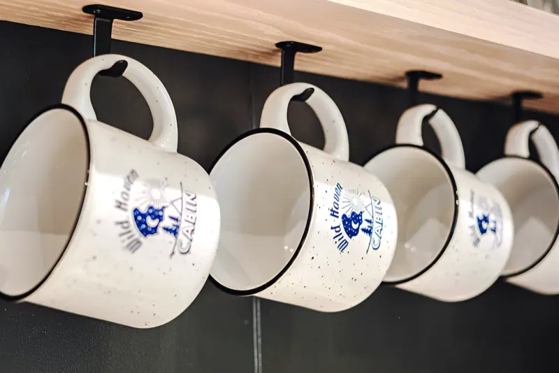 Speckled Wild Haven Cabin logo mugs hanging beneath a wood shelf